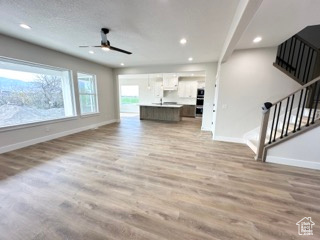 Unfurnished living room with light wood-type flooring, a ceiling fan, recessed lighting, and baseboards