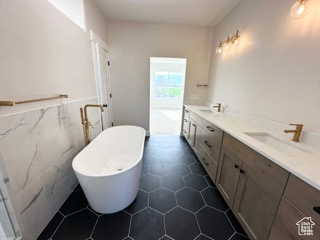 Bathroom featuring double vanity, a sink, a freestanding tub, and tile walls