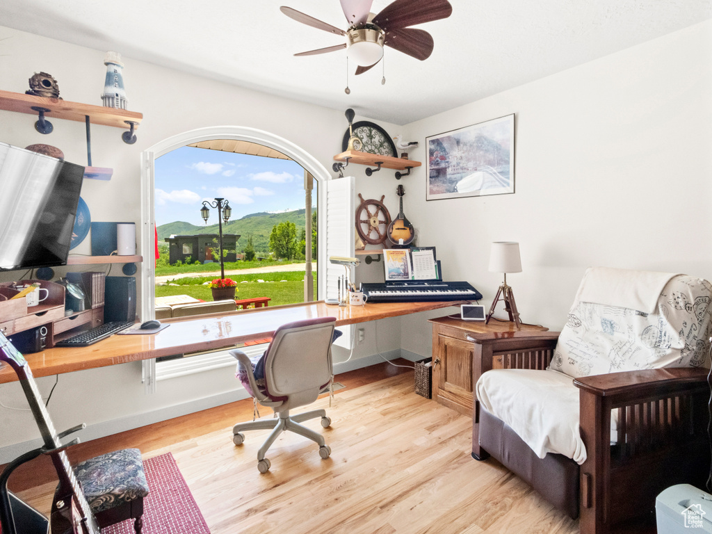 Office area with light wood-type flooring, baseboards, a ceiling fan, and built in desk