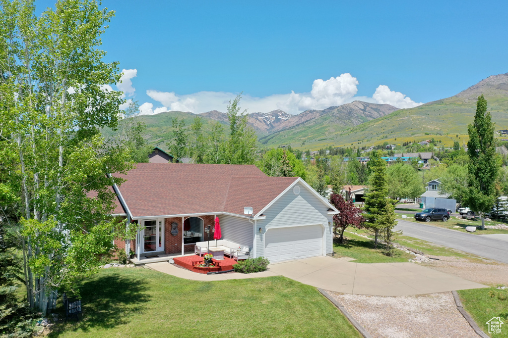Ranch-style house with a front lawn, a mountain view, driveway, covered porch, and a garage