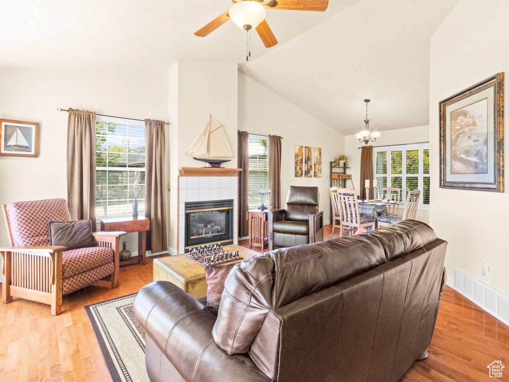 Living room with visible vents, light wood-style floors, high vaulted ceiling, ceiling fan with notable chandelier, and a fireplace