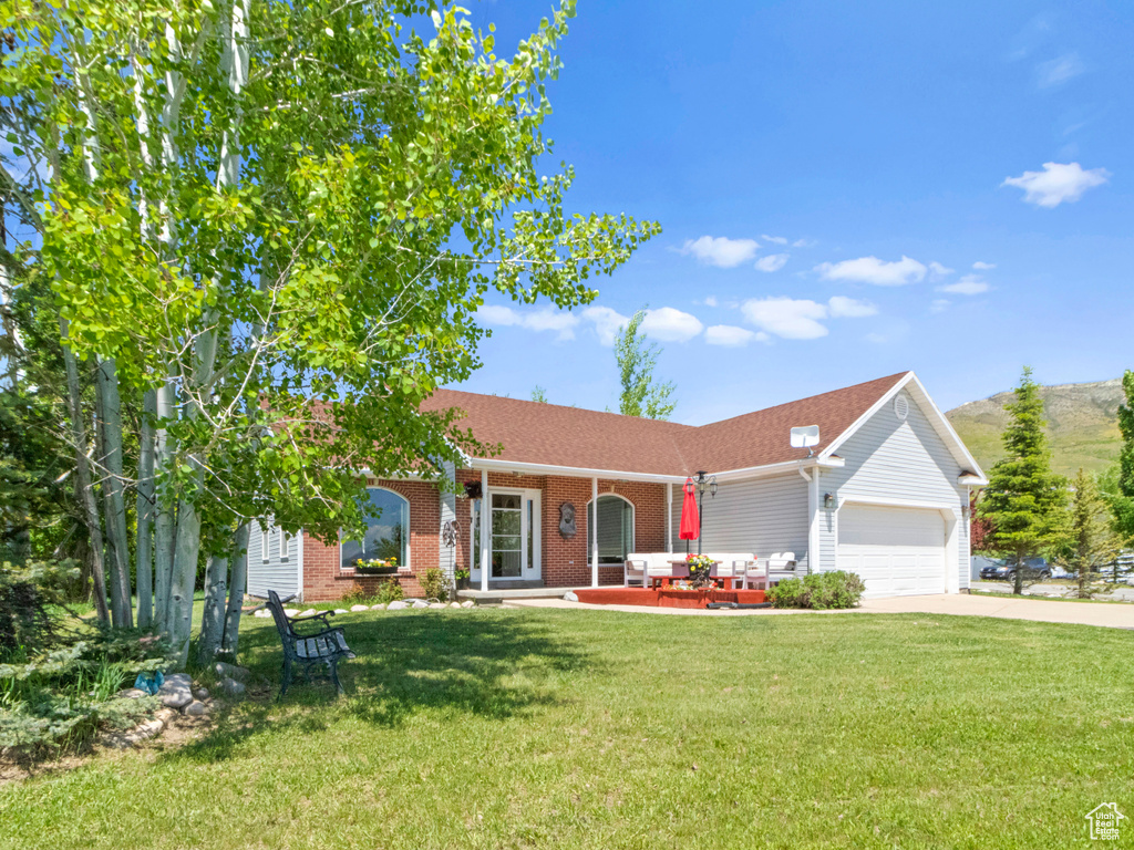Single story home with driveway, covered porch, an attached garage, a front yard, and brick siding