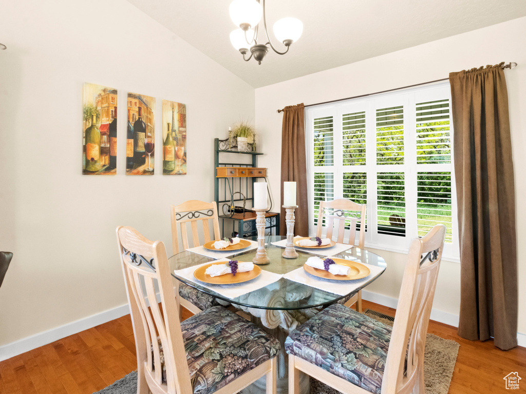 Dining room with wood finished floors, lofted ceiling, baseboards, and an inviting chandelier
