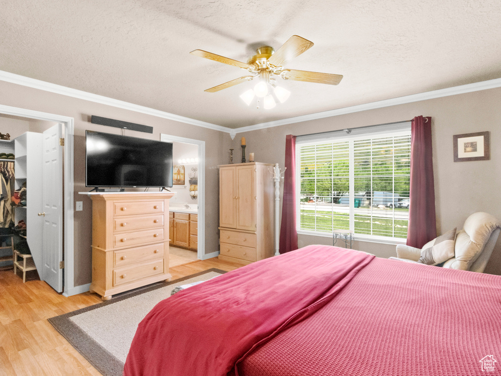 Bedroom with a walk in closet, light wood-type flooring, a textured ceiling, and crown molding