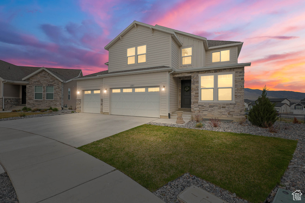 View of front of home with concrete driveway, a front lawn, stone siding, and a garage