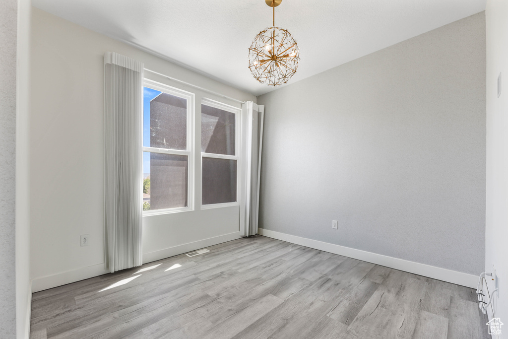 Unfurnished room featuring wood finished floors, a chandelier, and baseboards