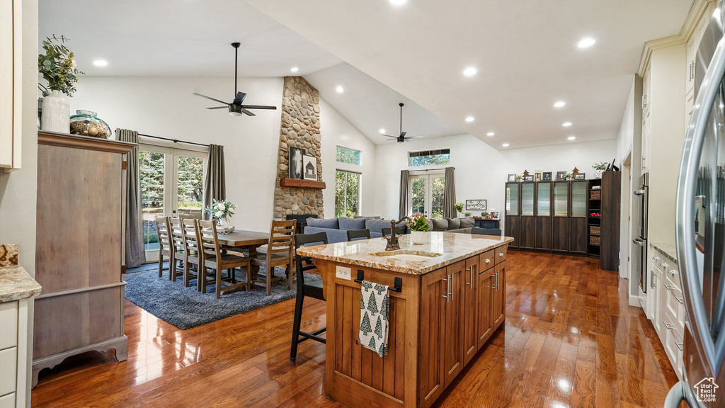 Kitchen with ceiling fan, open floor plan, a stone fireplace, brown cabinetry, and high vaulted ceiling