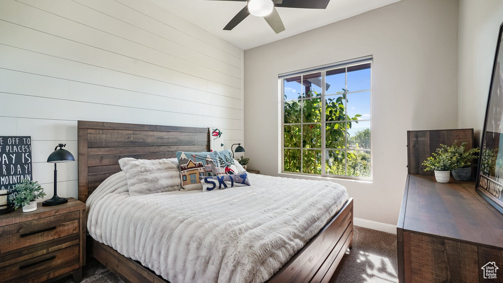 Bedroom featuring dark carpet, wooden walls, and a ceiling fan