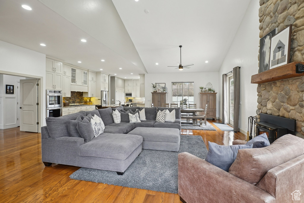 Living area with a stone fireplace, wood finished floors, ceiling fan, high vaulted ceiling, and recessed lighting