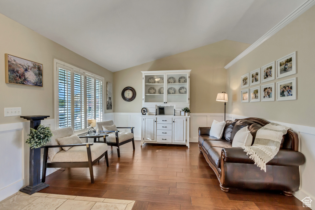 Living area with vaulted ceiling, dark wood-style flooring, a wainscoted wall, and crown molding