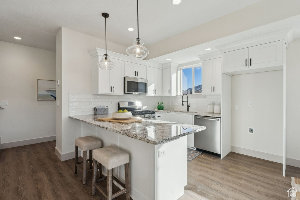 Kitchen with light stone counters, a peninsula, white cabinets, and appliances with stainless steel finishes