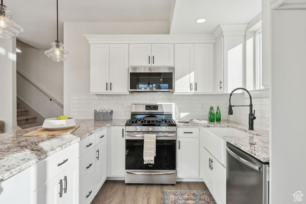Kitchen with light stone countertops, light wood-style flooring, stainless steel appliances, a sink, and white cabinetry