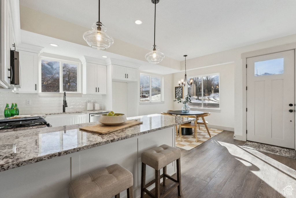 Kitchen featuring light stone countertops, a sink, light wood-style floors, a kitchen breakfast bar, and backsplash