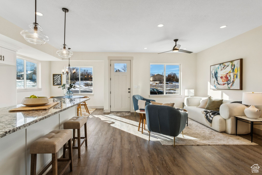 Living area with recessed lighting, dark wood-style flooring, baseboards, and ceiling fan with notable chandelier