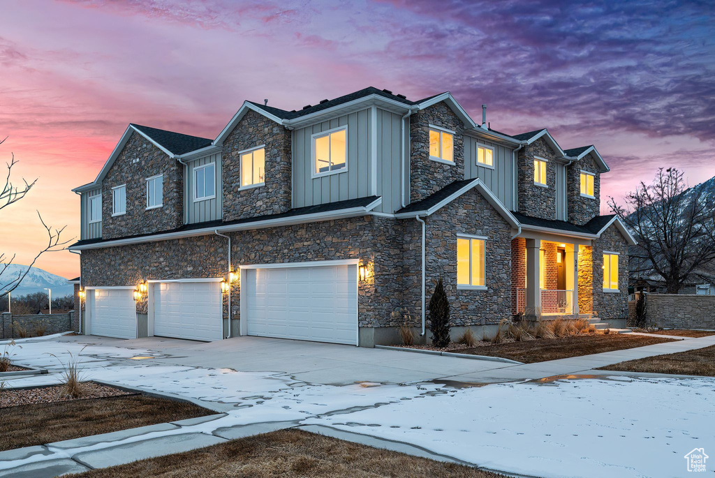 View of front of home with driveway, board and batten siding, an attached garage, and stone siding