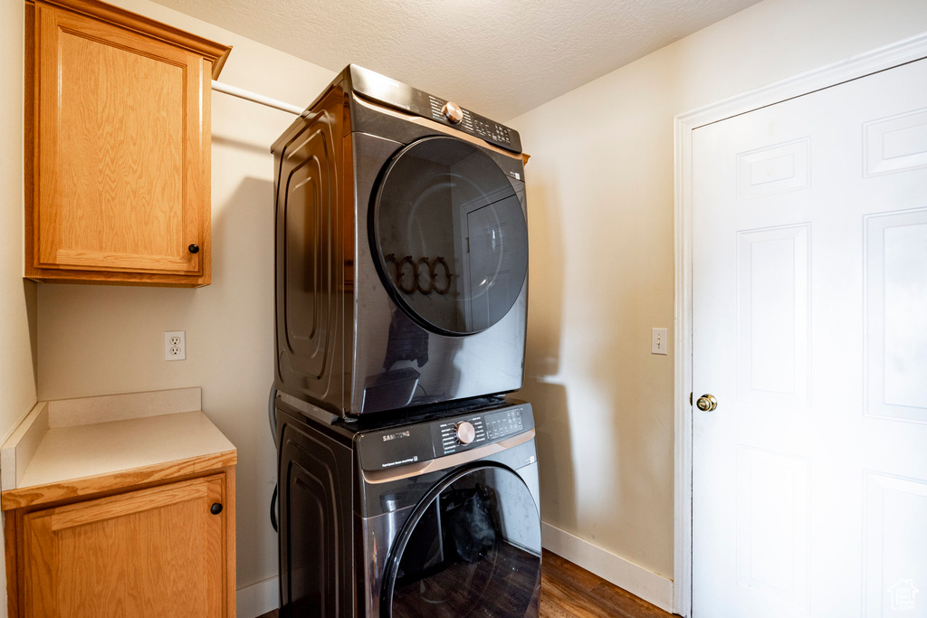 Laundry room with stacked washer / dryer, cabinet space, dark wood-style flooring, baseboards, and a textured ceiling