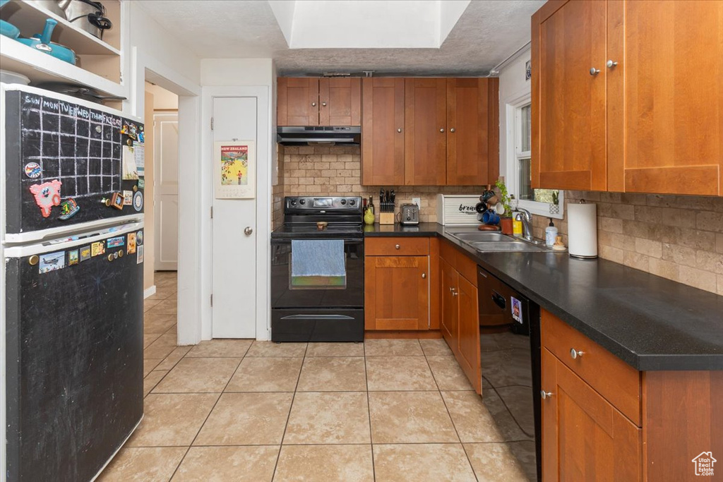 Kitchen with black appliances, brown cabinets, under cabinet range hood, and tasteful backsplash