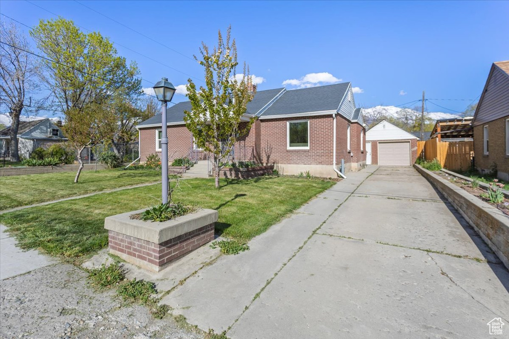 Bungalow featuring a front lawn, an outbuilding, brick siding, concrete driveway, and fence