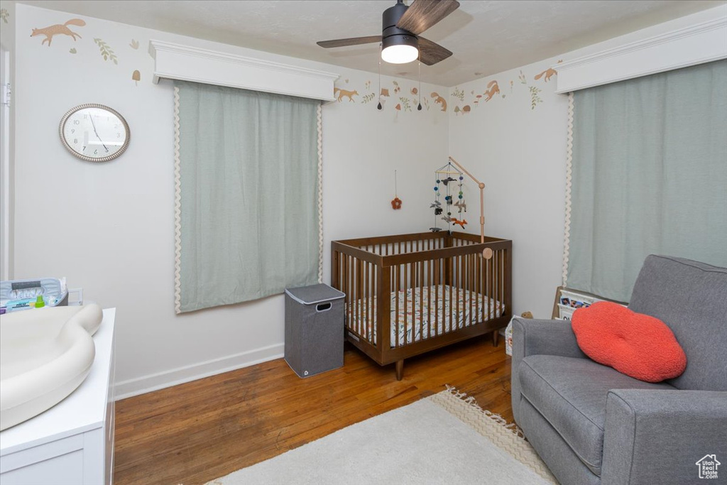 Bedroom with wood finished floors, ceiling fan, baseboards, and a crib