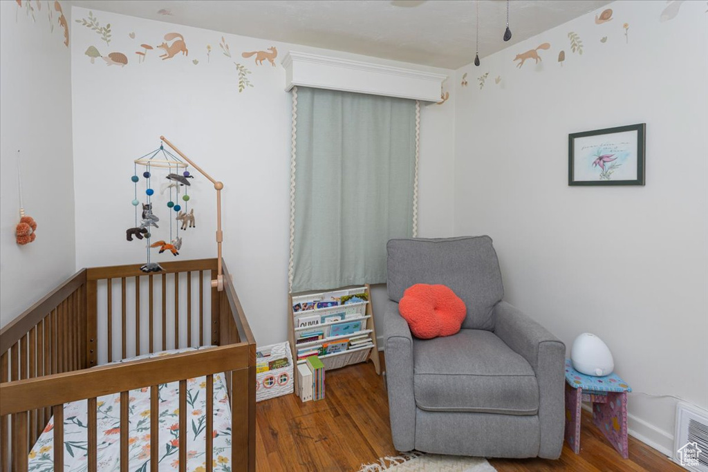 Bedroom with visible vents, a nursery area, and wood finished floors