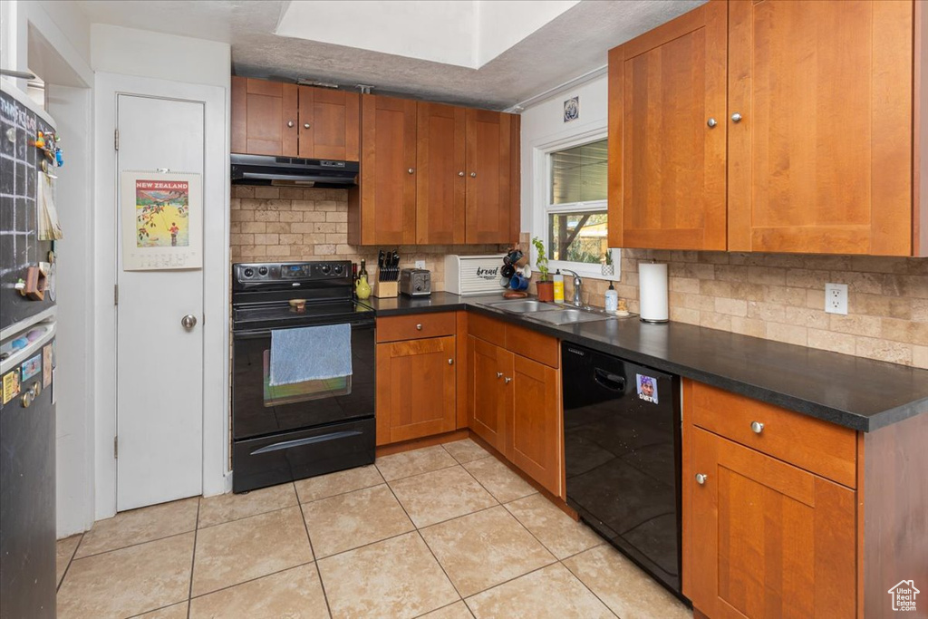 Kitchen featuring brown cabinets, tasteful backsplash, a sink, under cabinet range hood, and black appliances