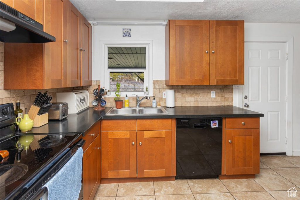 Kitchen featuring decorative backsplash, brown cabinetry, under cabinet range hood, black appliances, and a sink