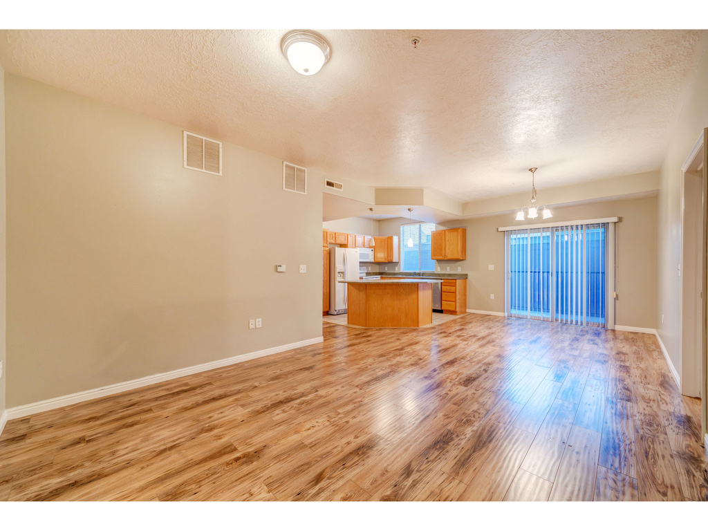 Unfurnished living room with a chandelier, light wood finished floors, a textured ceiling, and baseboards