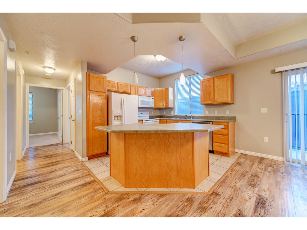 Kitchen with white appliances, light wood-type flooring, a center island, baseboards, and hanging light fixtures