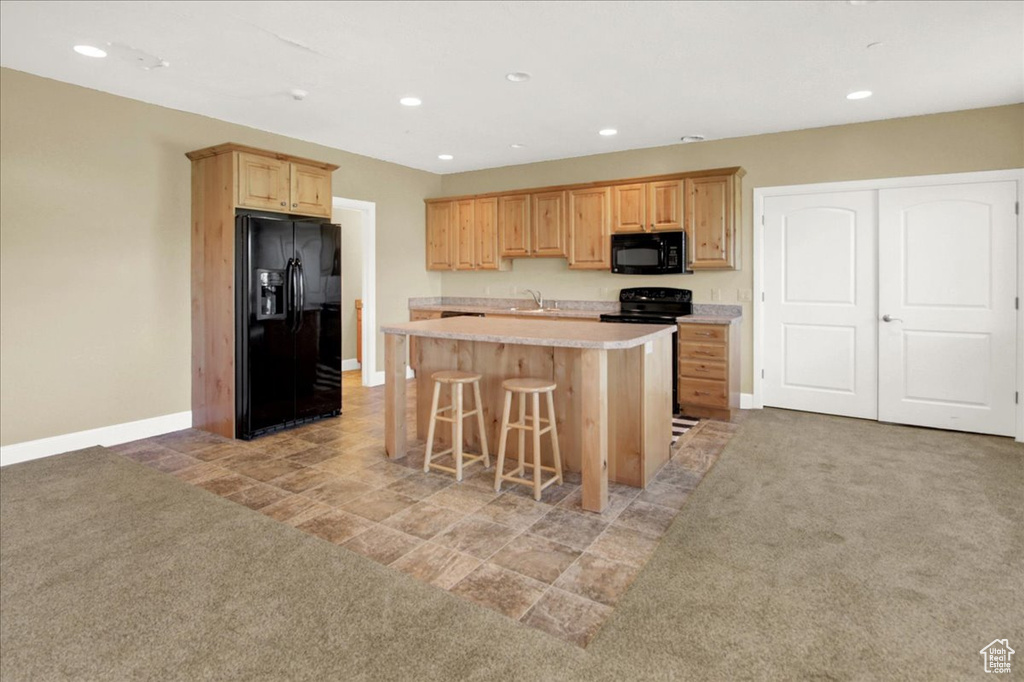Kitchen with a sink, light countertops, a center island, black appliances, and baseboards