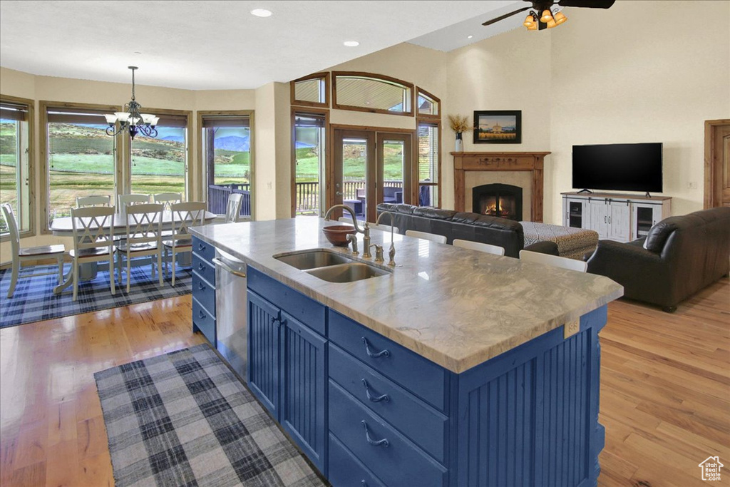 Kitchen featuring a sink, light wood-style floors, a warm lit fireplace, blue cabinets, and open floor plan