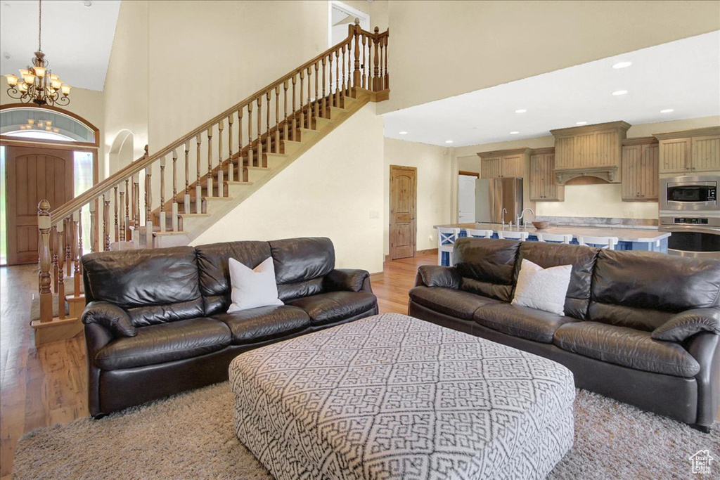 Living area with a chandelier, stairs, light wood-style floors, and a towering ceiling