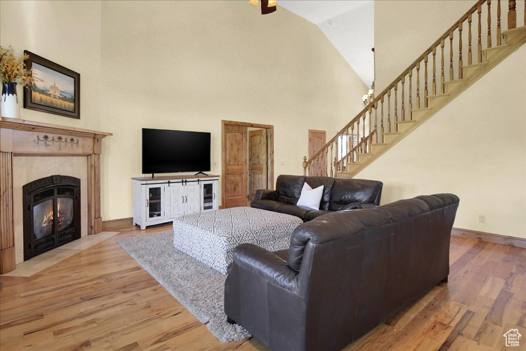 Living room featuring a premium fireplace, stairway, high vaulted ceiling, baseboards, and wood finished floors
