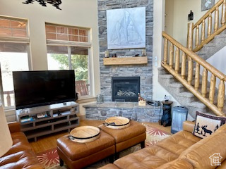 Living area with wood finished floors, a stone fireplace, and stairway