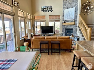 Living room featuring stairs, wood finished floors, a stone fireplace, and a high ceiling