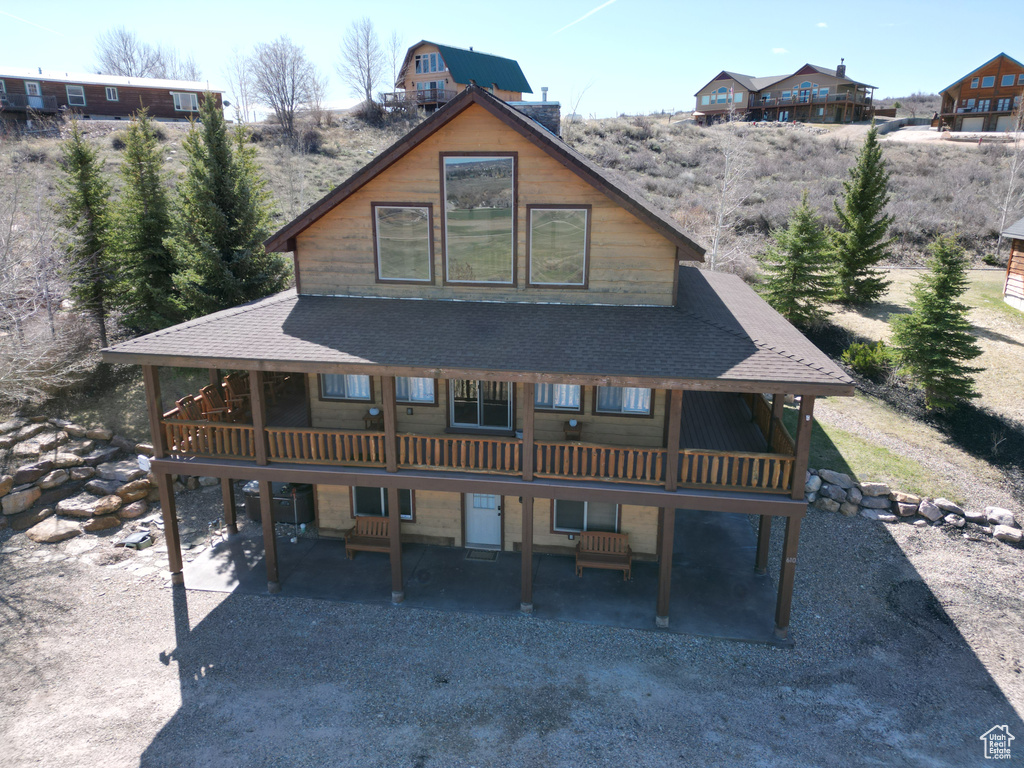 Back of property with a wooden deck, a patio area, and roof with shingles