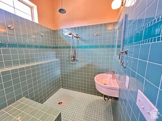 Bathroom featuring tile patterned flooring, tile walls, a sink, and tiled shower