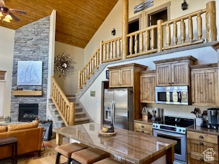 Kitchen with stainless steel appliances, a ceiling fan, a fireplace, wooden ceiling, and high vaulted ceiling