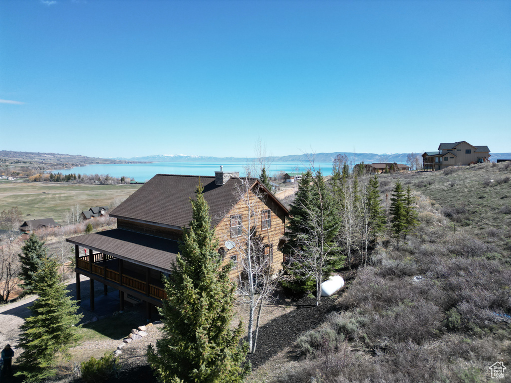 View of side of home with roof with shingles and a deck with water view