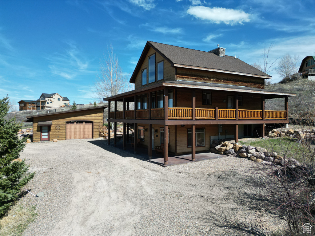 Back of house with a wooden deck, driveway, and an outbuilding