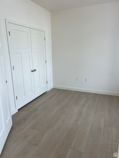 Unfurnished bedroom with a closet, wood finished floors, and baseboards