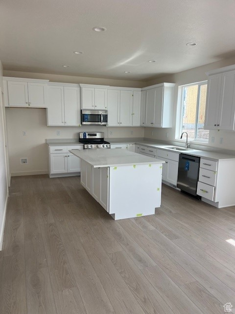 Kitchen featuring a sink, stainless steel appliances, light wood-style flooring, a kitchen island, and white cabinets