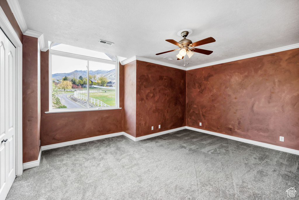 Empty room featuring crown molding, baseboards, carpet floors, a mountain view, and a ceiling fan