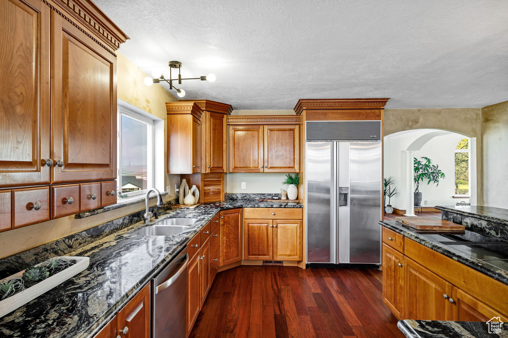 Kitchen with dark stone countertops, brown cabinetry, stainless steel appliances, a sink, and dark wood-type flooring