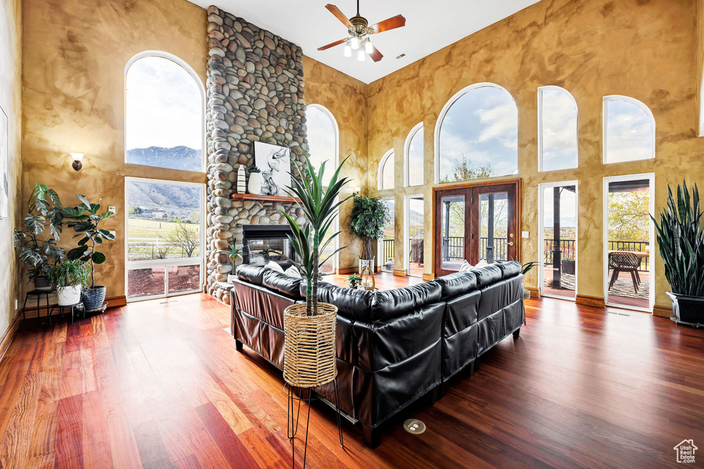 Living room with wood finished floors, ceiling fan, a fireplace, and a towering ceiling