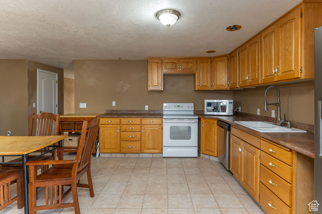 Kitchen with stainless steel appliances, brown cabinets, dark countertops, a sink, and a textured ceiling