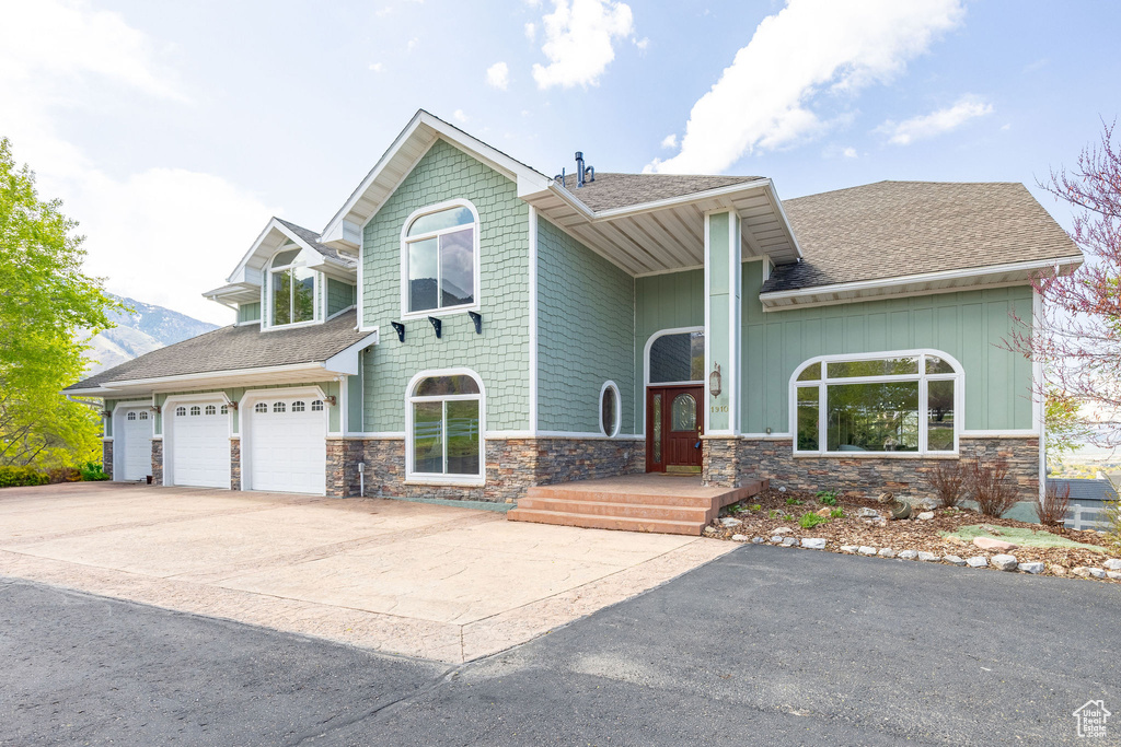 Craftsman-style home with roof with shingles, concrete driveway, board and batten siding, and stone siding