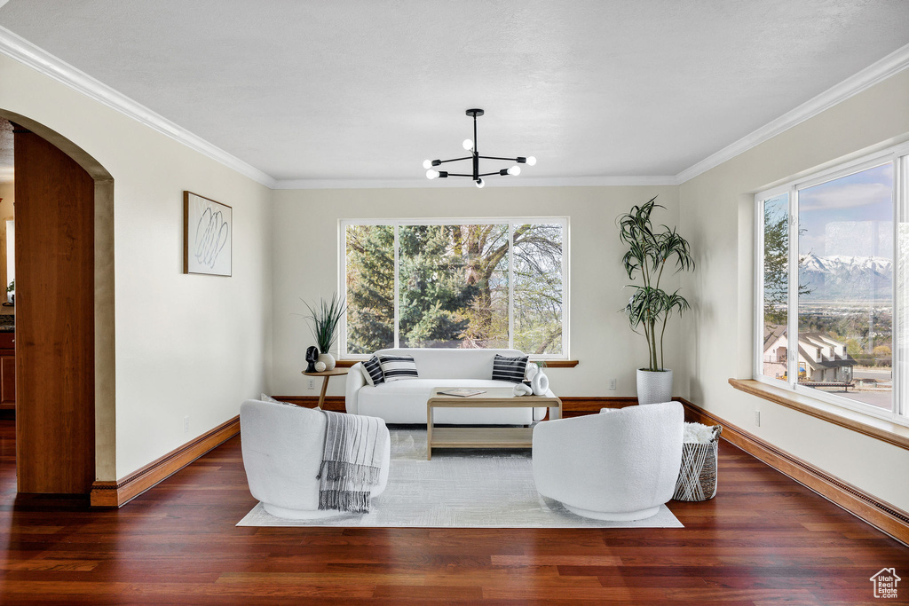 Living area with ornamental molding, a notable chandelier, wood finished floors, and arched walkways
