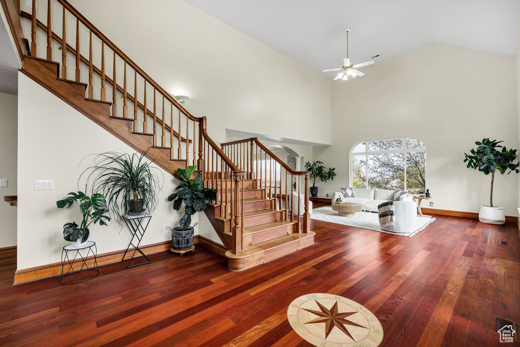 Staircase with high vaulted ceiling, a ceiling fan, visible vents, baseboards, and wood finished floors