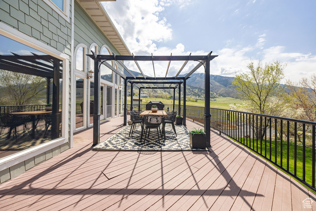 Wooden terrace featuring a mountain view, outdoor dining space, and a pergola