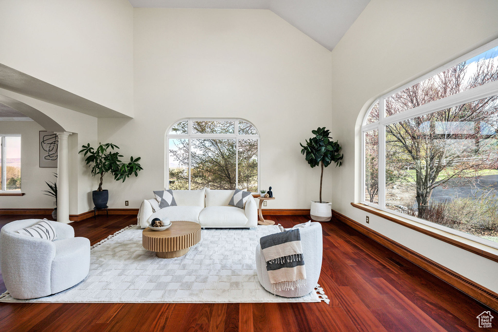 Living room with arched walkways, high vaulted ceiling, baseboards, and ornate columns